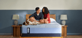 A man and woman sitting on a Posturepedic Hybrid mattress with their dog